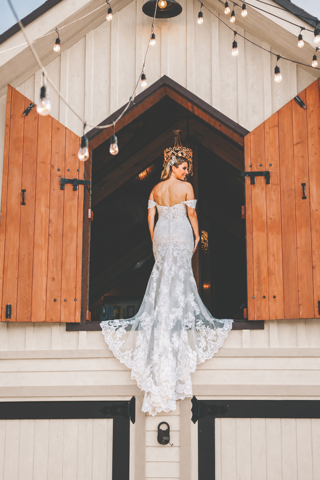 Bride standing beneath string lights in the open barn window at The Arbor Estate