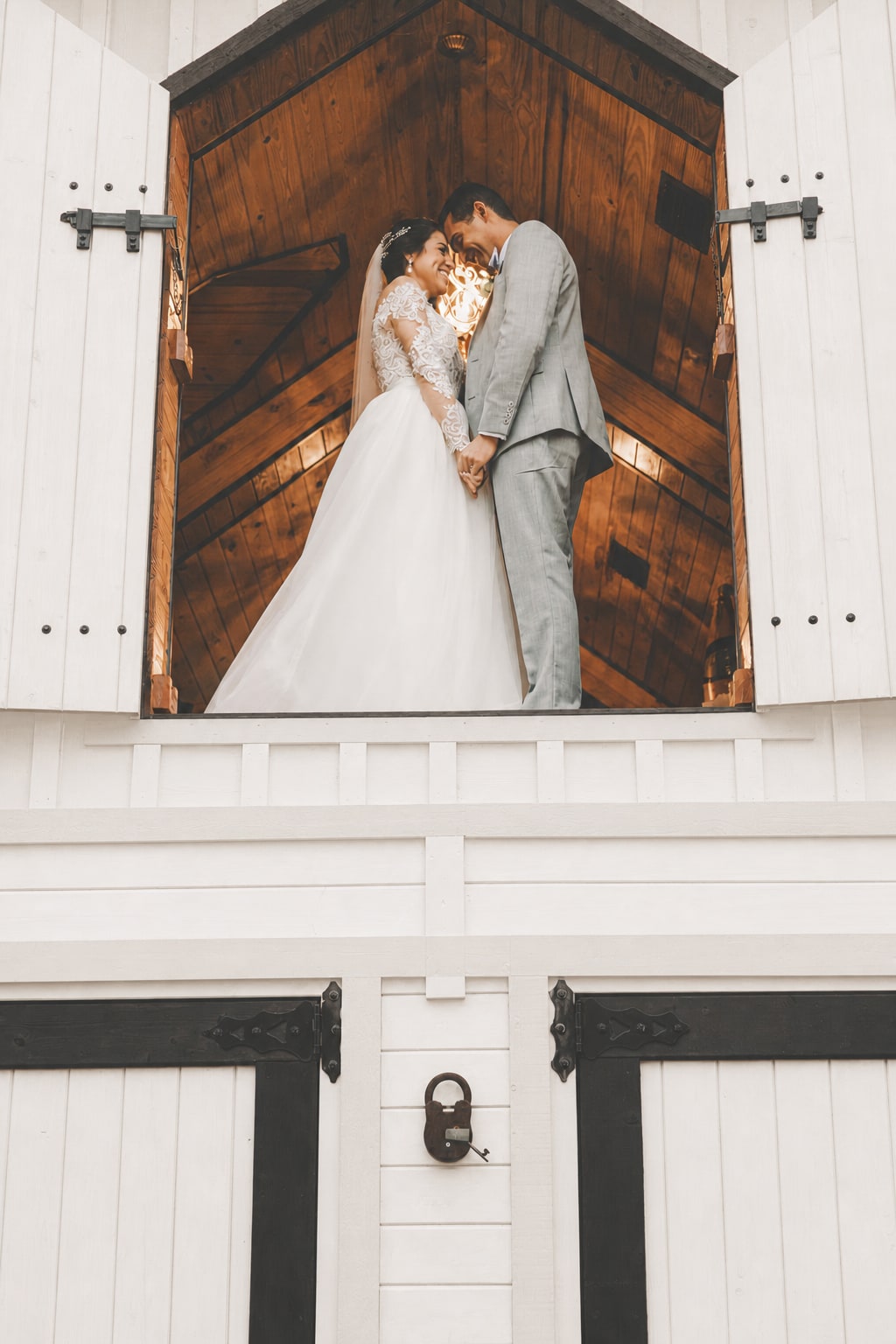 Newlyweds standing together in the open upper doorway of the estate's signature white building